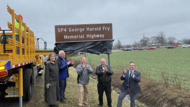 Photo of elected officials and family members in front of highway sign
